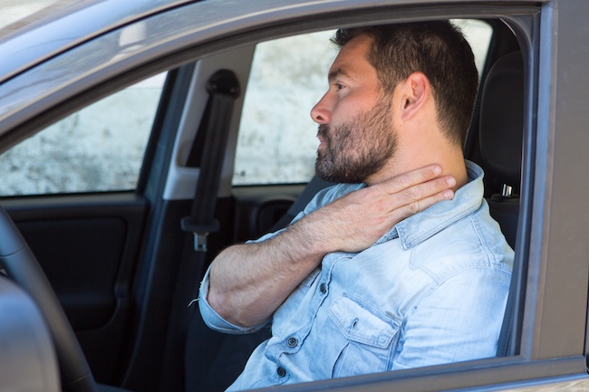 Man in car holding neck, indicating injury after rear-end collision, relevant to Buford car accident legal representation.