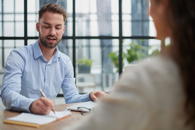 Young male attorney consulting with a client in a modern office setting, discussing personal injury case details and taking notes.