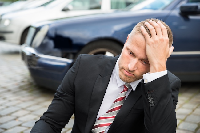 Man in a suit sitting on the ground with a distressed expression, surrounded by parked cars, reflecting the emotional aftermath of a car accident and the need for legal assistance in Marietta, Georgia.
