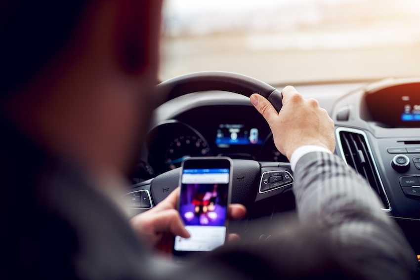 Person in a car using a smartphone while driving, illustrating distracted driving, a significant issue in Buford, Georgia.