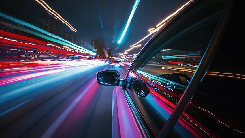 Car speeding through city streets at night, blurred lights conveying high velocity, emphasizing the dangers of speeding accidents.