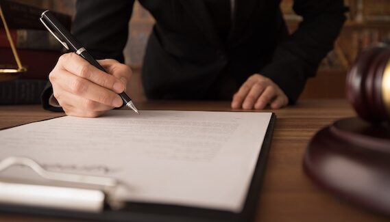 Lawyer signing legal documents on a wooden desk with a gavel and law books, representing personal injury law and legal assistance for texting while driving accident cases.