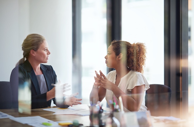Two women in a professional setting discussing legal matters, with documents and a notepad on the table, representing a consultation for personal injury claims after a rear-end collision.