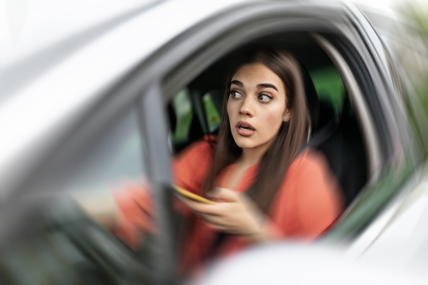 Distracted driver in a car looking alarmed while holding a smartphone, illustrating the dangers of distracted driving in Buford, Georgia.