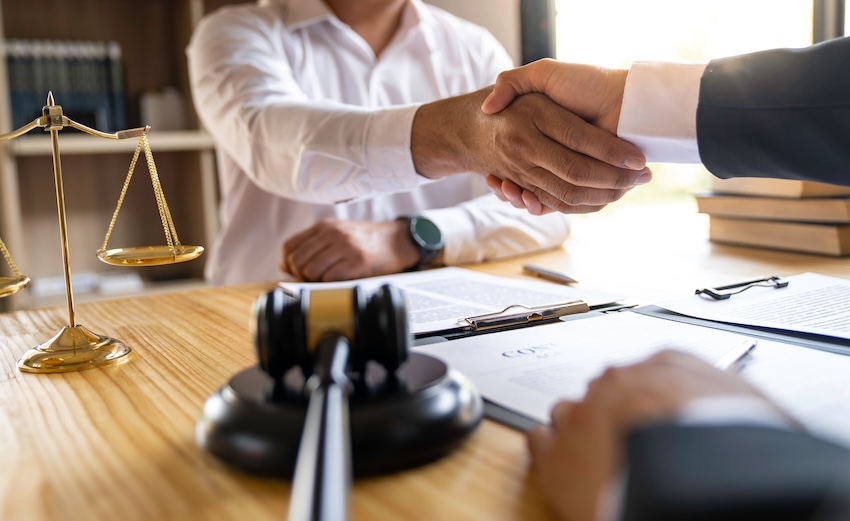 Lawyer and client shaking hands in a legal consultation setting, with a gavel and scales of justice on the table, representing legal support for distracted driving accident victims in Buford, Georgia.