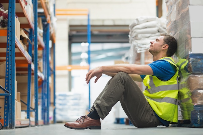 Individual in safety vest sitting on warehouse floor, appearing distressed, surrounded by shelves of goods, illustrating the impact of workplace accidents and personal injury claims.