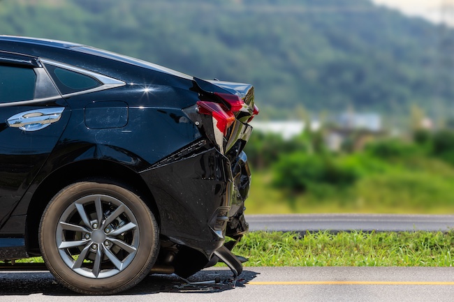 Black car with rear-end damage on roadside, illustrating the aftermath of a rear-end collision, relevant to Buford car accident legal services.