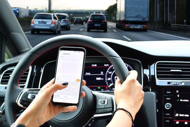 Person texting on smartphone while driving, showcasing distracted driving in a busy traffic environment, emphasizing dangers of texting while driving.