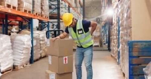 An example of warehouse workers needing workers compensation in Cumming, Georgia: a worker bends over a stack of boxes while in pain from injuring their back on the job.