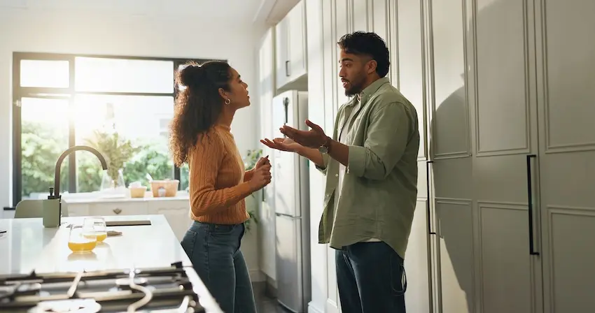 A couple is having a serious discussion in a modern kitchen about responsibility and insurance claims following a shared fault accident in Georgia.