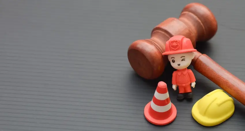 A wooden judge's gavel is resting beside a small figurine of a worker in a hard hat a traffic cone and a yellow construction helmet symbolizing the legal and medical process of filing a workers' comp physician-supported injury claim at the Law Offices of Humberto Izquierdo Jr. PC in Georgia.