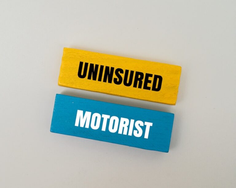Two painted wooden blocks stacked on a white surface one yellow reading "UNINSURED" and one blue reading "MOTORIST" spelling out the term uninsured motorist to illustrate a critical area of auto insurance coverage for accident victims in Georgia who could use help from the Law Offices of Humberto Izquierdo Jr. PC.