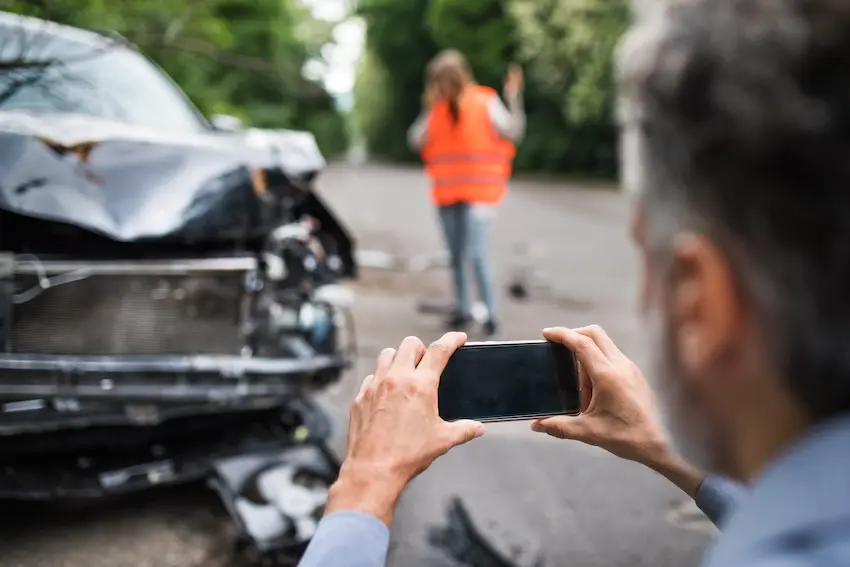 Person photographing vehicle damage at the scene of a Georgia car accident to document evidence without a police report